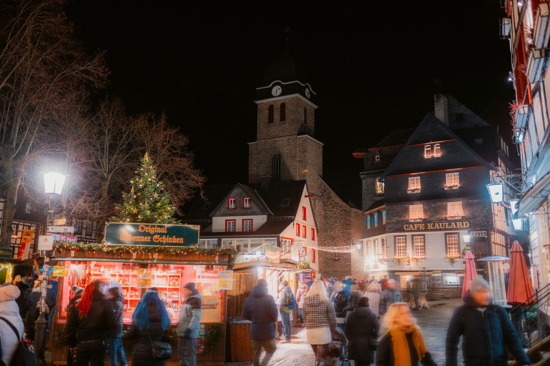 Hell erluchtete Buden des Weihnachsmarkts Monschau mit Fachwerkhäusern im Hintergrund