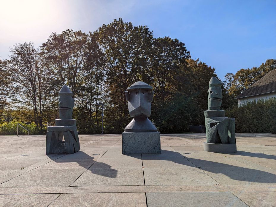 De driedelige bronzen sculptuur Lehrerkollegium einer Schule für Totschläger van Max Ernst staat voor de ingang van het museum.