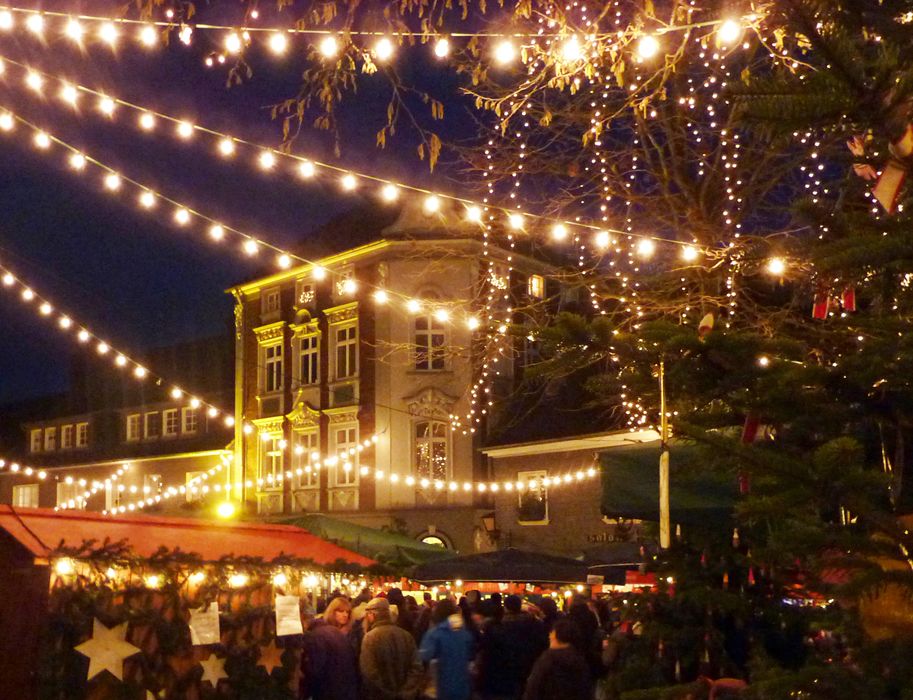 Vor einem Fachwerkhaus hängen Lichterkettenüber den Buden des Weihnachtsmarktes